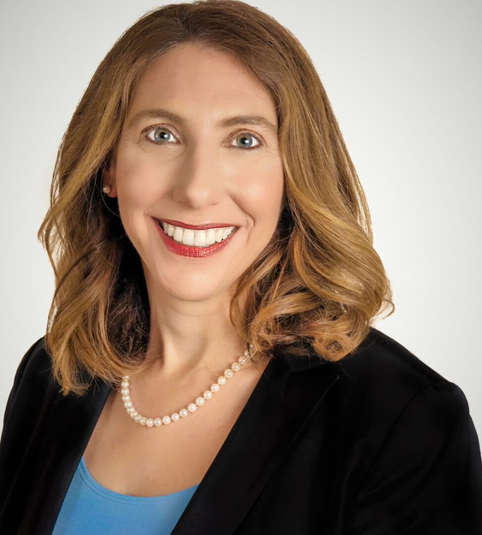 Smiling woman in black blazer and pearls.